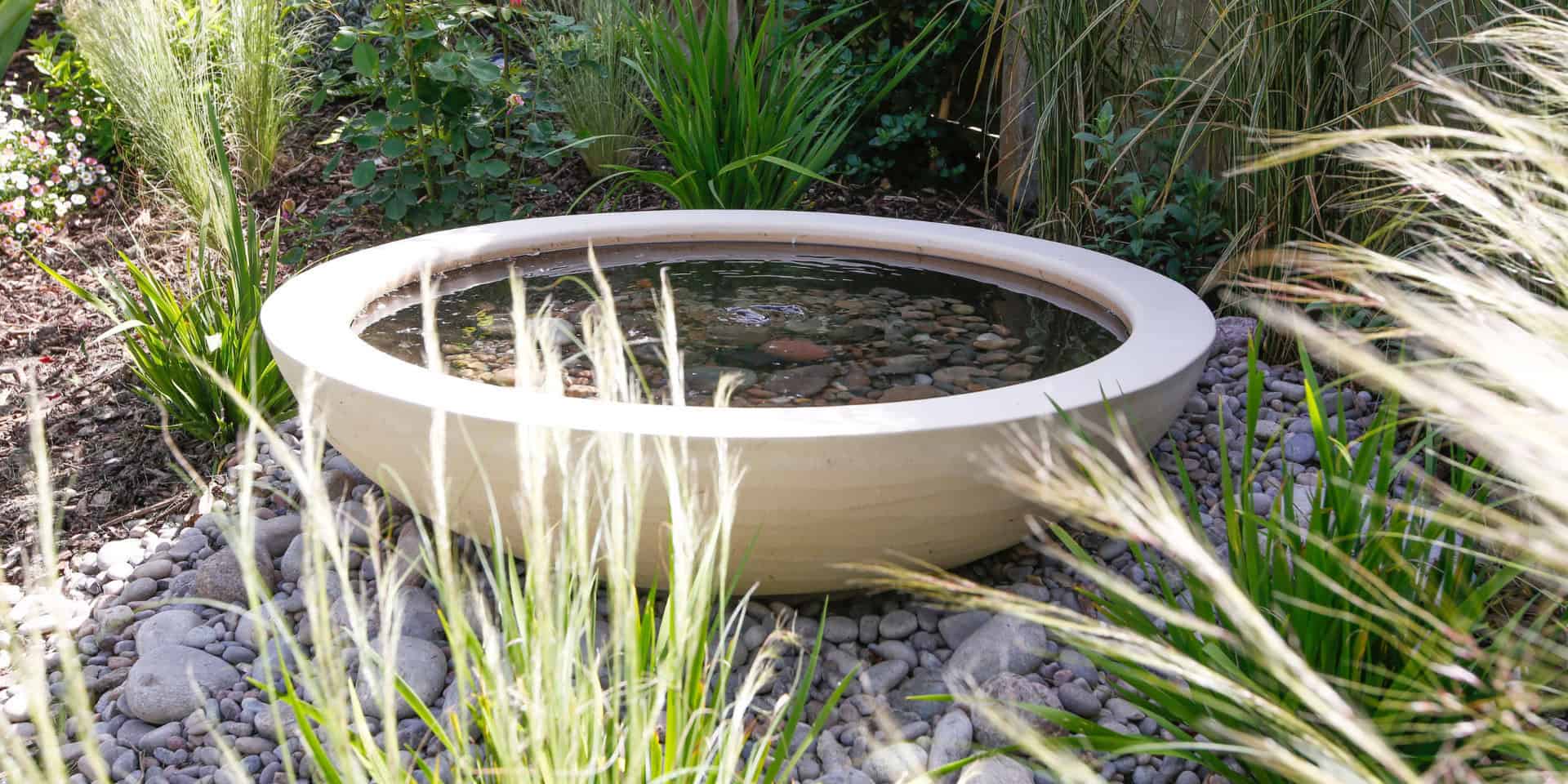 Urbis Lily bowl installed by Heartwood Garden Design in a harpenden garden. A beautiful shallow coloured water feature on a base of pebbles and filled with a layer of pebbles and the gentle movement of water.
